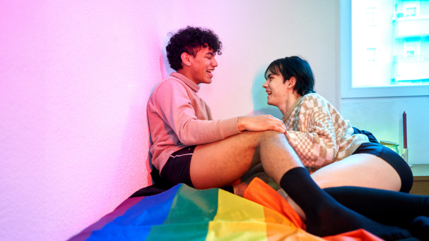 Two people having a lively conversation while sitting on a Pride flag.