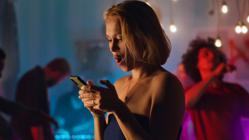 Woman gasping at her phone while at a dance club.