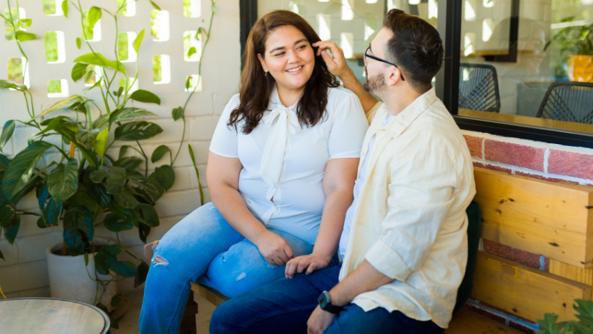 Man gently brushing back his partner’s hair while smiling in a sunroom.