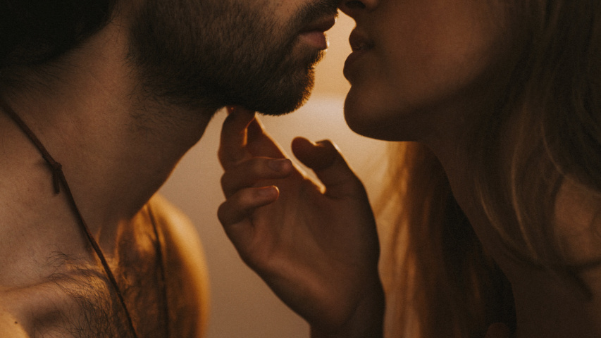 Woman placing her hand against her partner’s chin as they lean in to kiss one another amid a soft glow.
