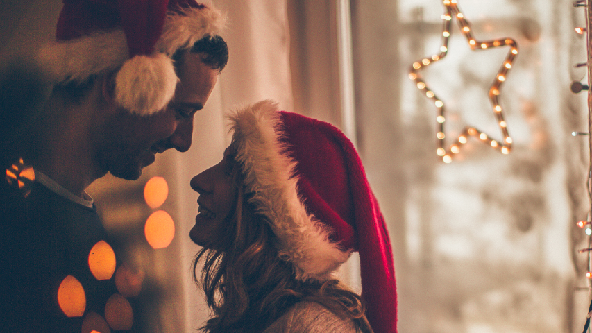 Un couple portant des bonnets de père Noël se rapproche pour un baiser de Noël.