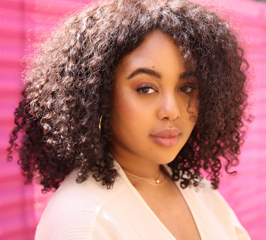 Headshot of Shadeen posing for the camera in front of a pink gate