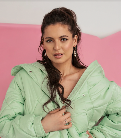 Headshot of Karine posing for the camera in front of a white and pink backdrop