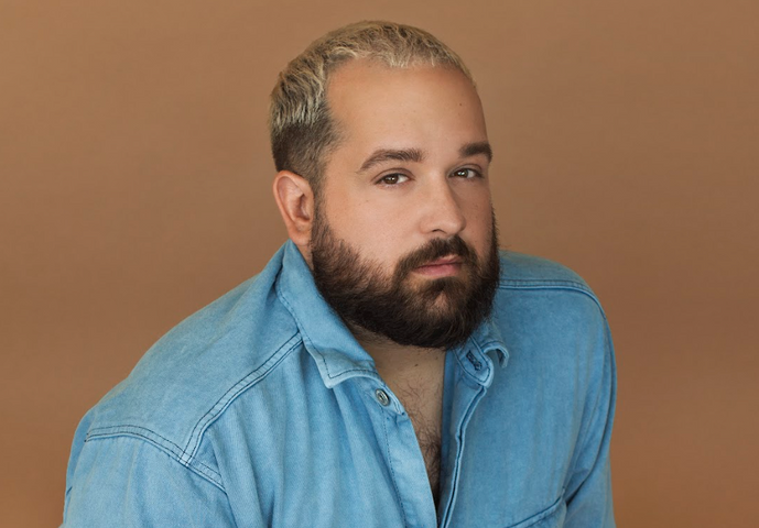 Karl Hardy en chemise de denim qui prend la pose devant un arrière-plan brun.