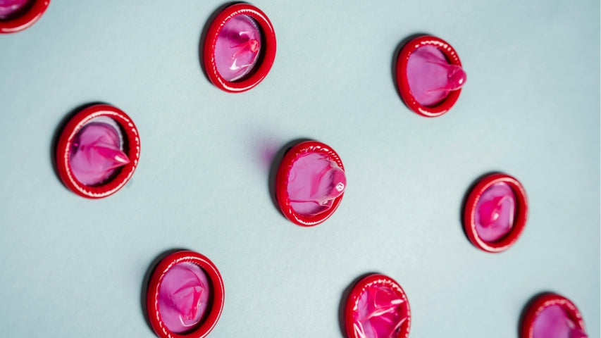 Des rangées de condoms roses et rouges étalées sur un tableau blanc.