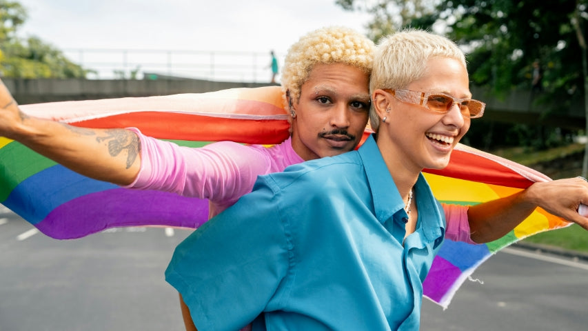 Two people on an empty street holding a Pride flag behind them.