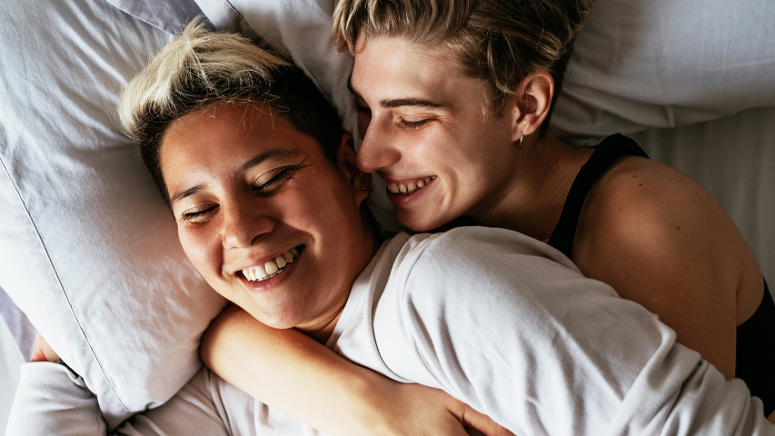 Un couple heureux enlacé dans un lit.