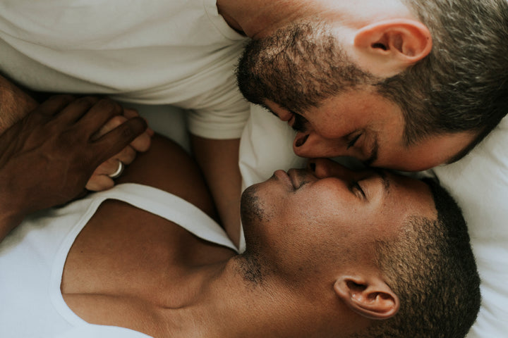 A happy couple lays close together in bed, holding hands.