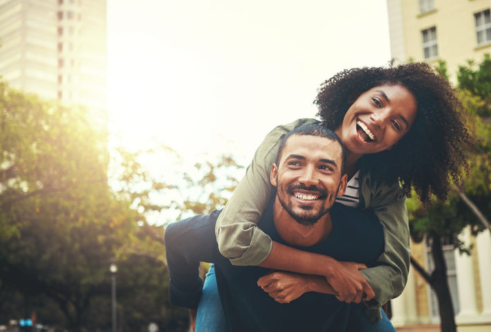 Une femme sur le dos de son partenaire souriant en public.