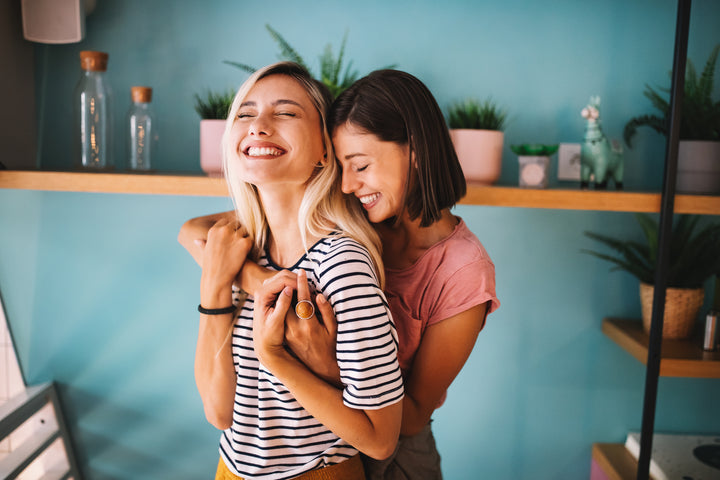 Two girls holding each other closely while laughing in a room full of plants