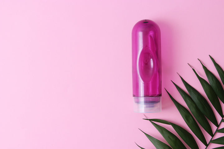 A pink bottle of lubricant and a green palm leaf on a pink background.