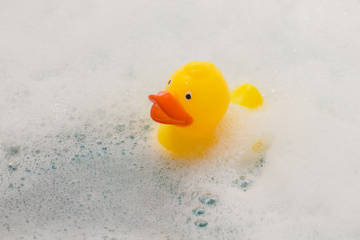 A yellow rubber duck floats in a bubble bath.