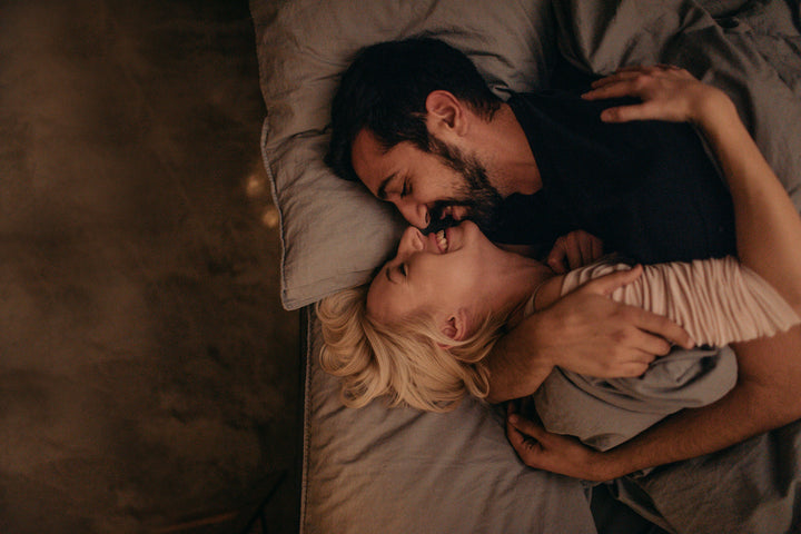 Woman laughing while her partner is smiling and holding her tightly under the bed covers