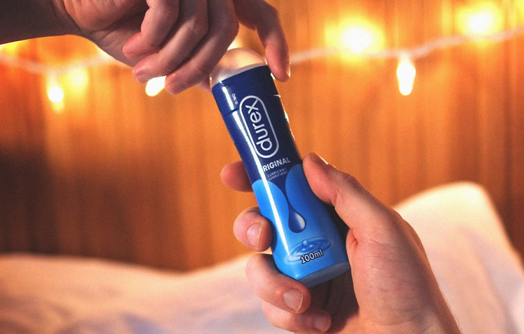 Des mains qui tiennent une bouteille de lubrifiant Durex Original devant des guirlandes lumineuses.