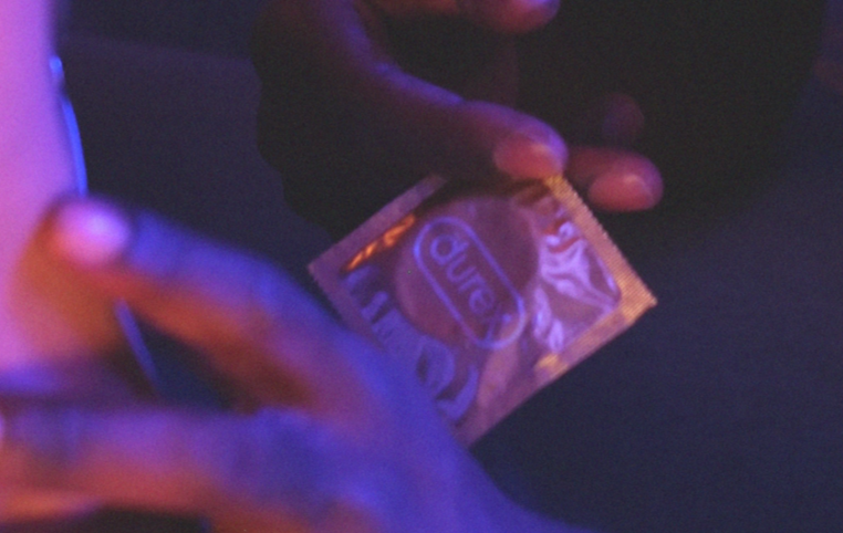 A hand holds a Durex condom wrapper in moody lighting.