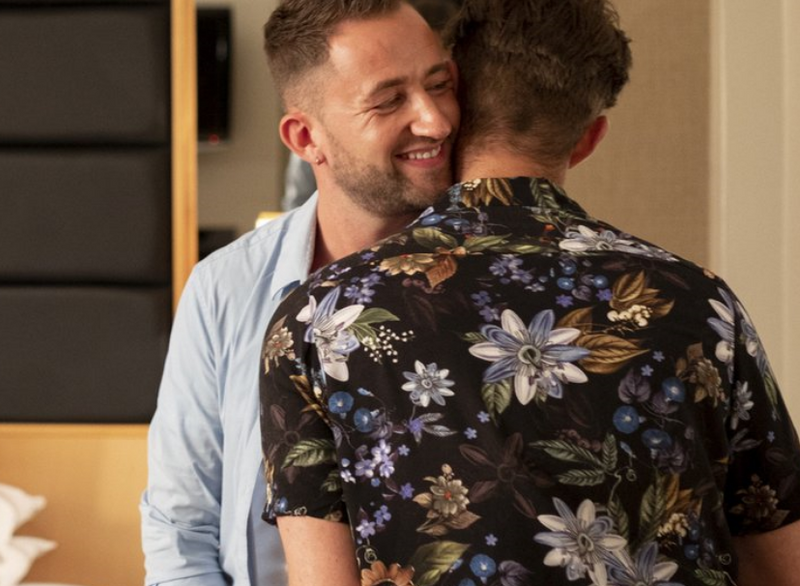 Man smiling into the neck of his partner wearing a floral shirt