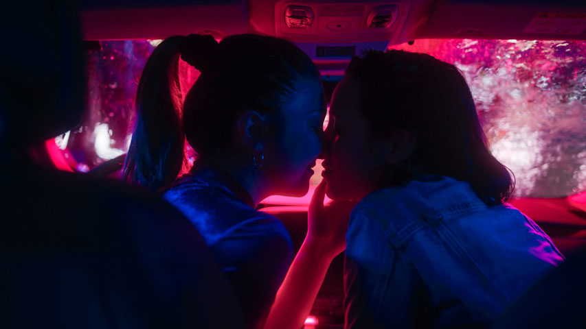 Partners going in for a kiss in their car while warm lighting illuminates them.