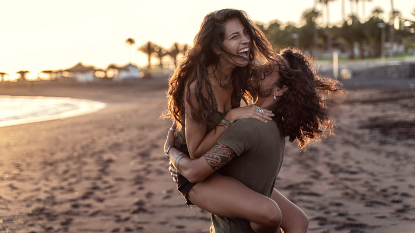 Man lifting his girlfriend as she laughs on a tropical beach.