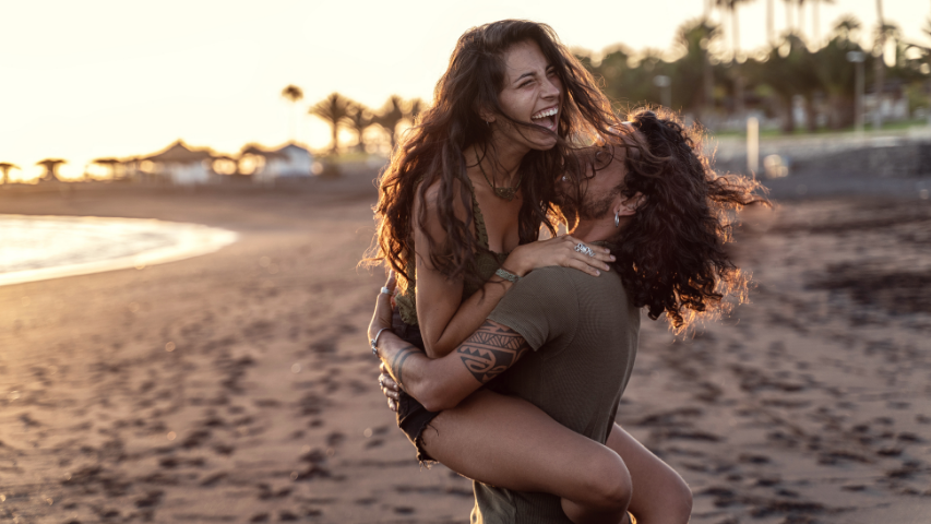 Homme qui soulève sa copine alors qu’elle rit sur une plage tropicale.