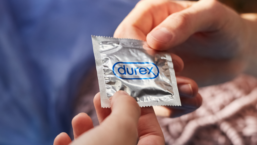 Deux mains tenant un condom Durex non déballé dans un emballage argenté.