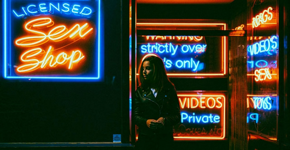 Woman waiting outside a vibrant sex shop with neon signage.