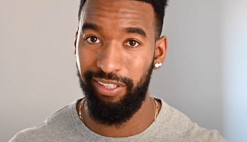 Malcolm wearing a grey shirt speaking into the camera