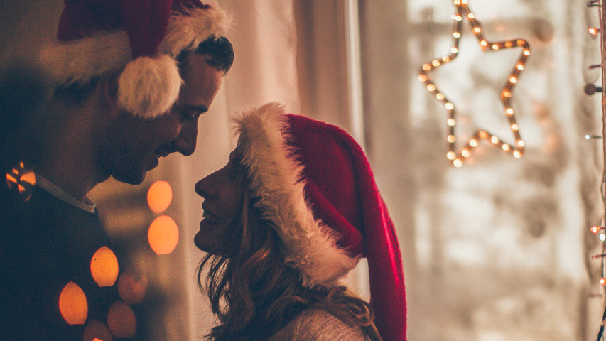 Couple wearing Santa hats getting closer to one another for a holiday kiss.