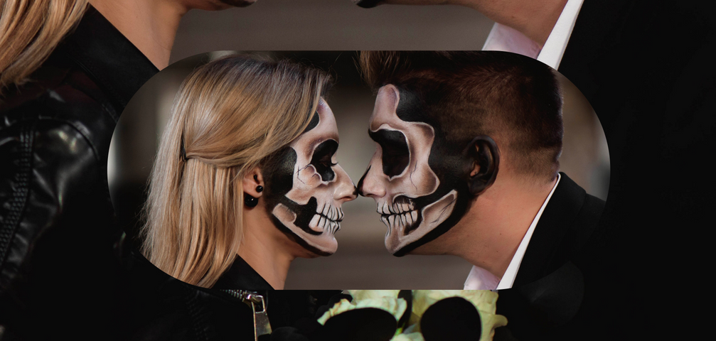 Two people wearing skull makeup leaning in for a Halloween peck