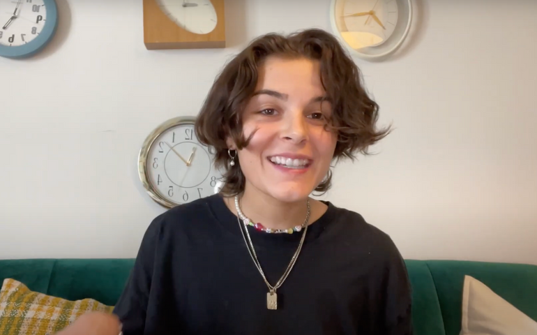 Rox Deragon sitting on the sofa wearing multiple necklaces and smiling into the camera