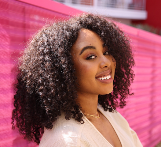 Portrait de Shadeen Francis adossée à une clôture rose et souriant à l’appareil photo.