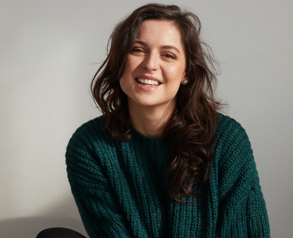 Headshot of Karine wearing a green sweater while smiling into the camera