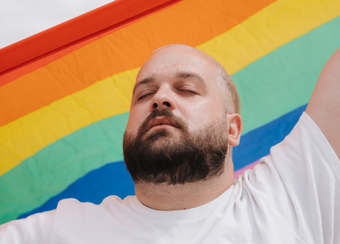 Karl Hardy, les yeux fermés, devant un drapeau de la Fierté.