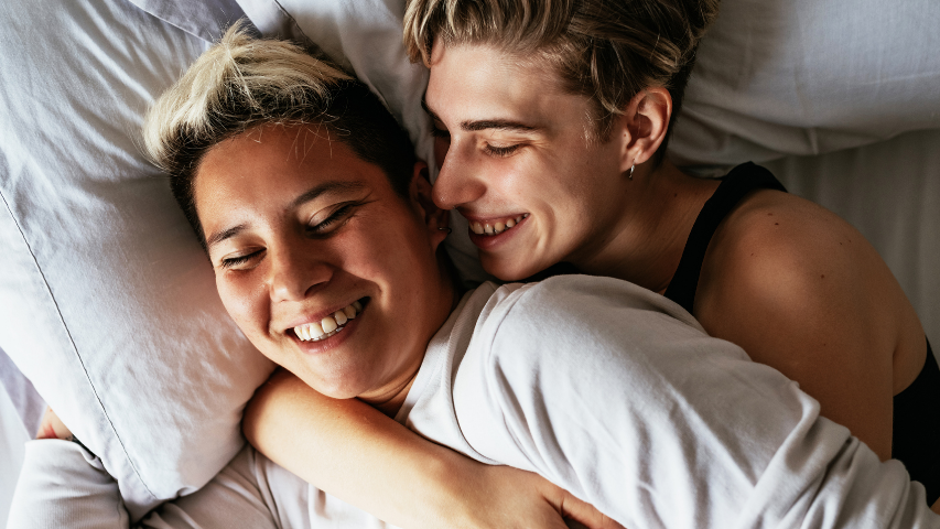 A couple happily cuddles in bed.