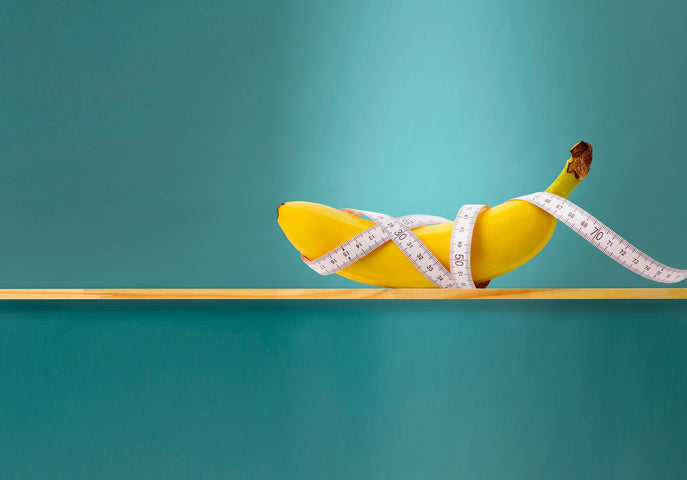 A banana with a white measuring tape around it on a blue background.