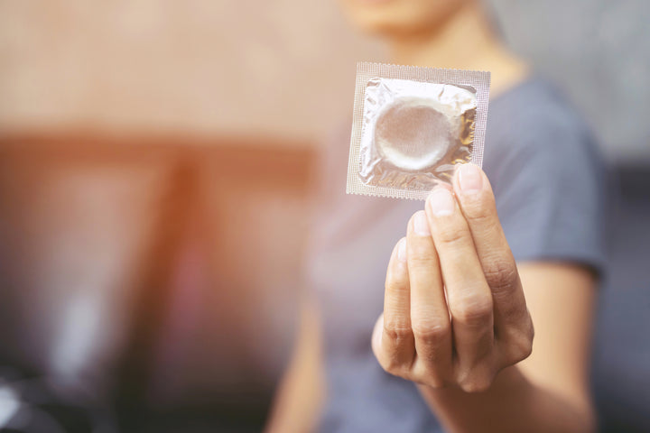 Une main tenant un condom dans son emballage devant l’appareil photo.