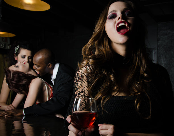 A woman bares her fangs while a man necks his partner in the background.