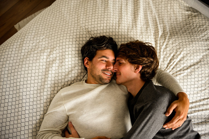 Deux hommes qui se cajolent et se sourient dans un lit.