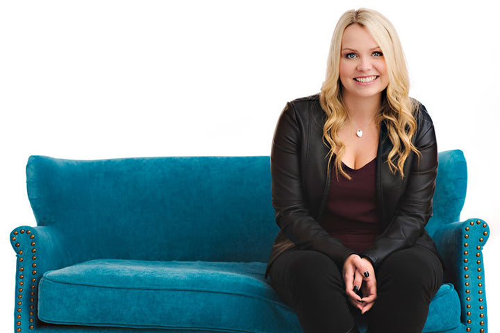 Lindsay Kenna sitting on a teal sofa while smiling into the camera