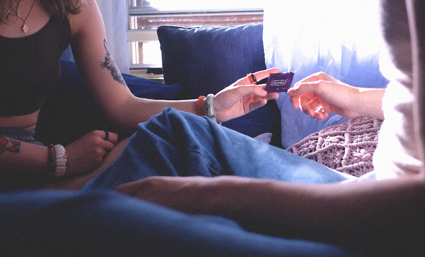 Des mains qui s’échangent un emballage violet de condom Durex.