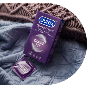 Boîte de condoms Durex Sensi-Thin à ajustement étroit et condom dans son emballage sur un drap de lit
