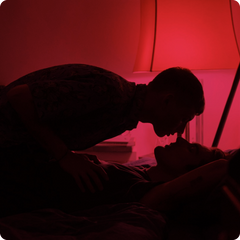 Couple’s silhouette in bed together, about to kiss, against a red light.