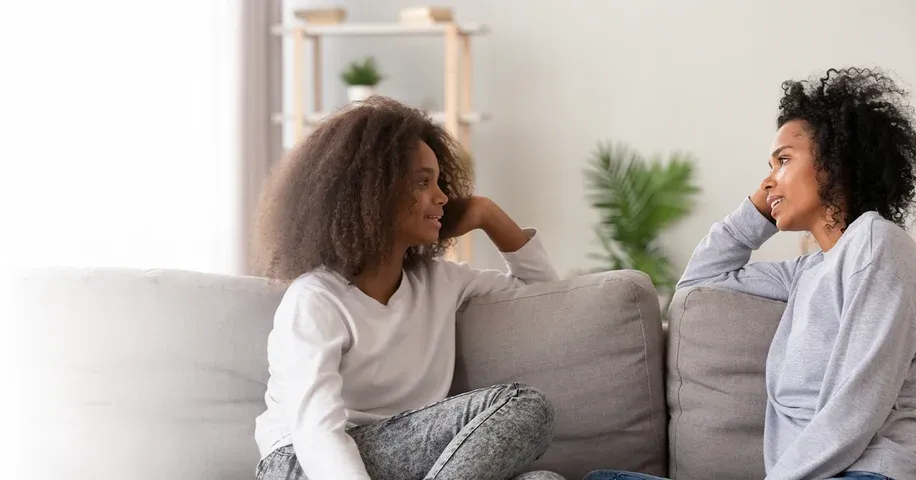 Une mère et sa fille, assises sur un sofa, discutent de santé sexuelle.