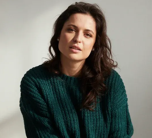 Headshot of Karine wearing a green sweater while posing for the camera